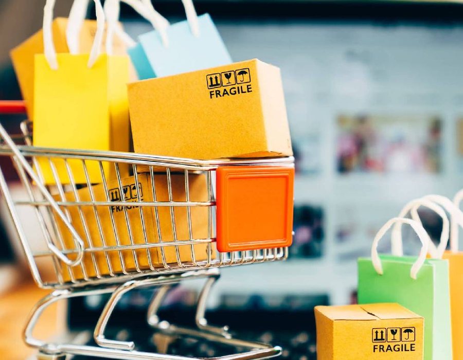 A shopping cart full of parcels and shopping bags in front of a laptop